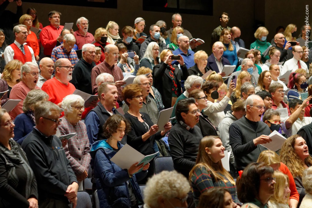 A group of audience members in a theater, singing.